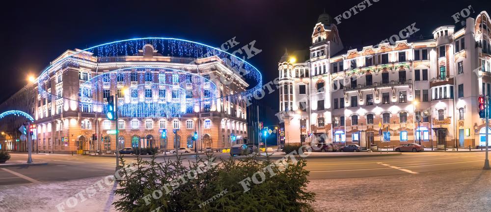 На фотографии изображена Австрийская площадь в Санкт-Петербурге, украшенная к Новому году. Здания на Каменноостровском проспекте сияют праздничной иллюминацией, создавая атмосферу радости и уюта. Световые гирлянды и декорации подчеркивают архитектурную красоту площади. Это место привлекает жителей и гостей города в преддверии Рождества.